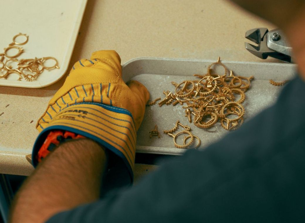 Gloved hand holding a tray full of gold ring clippings in a casting house
