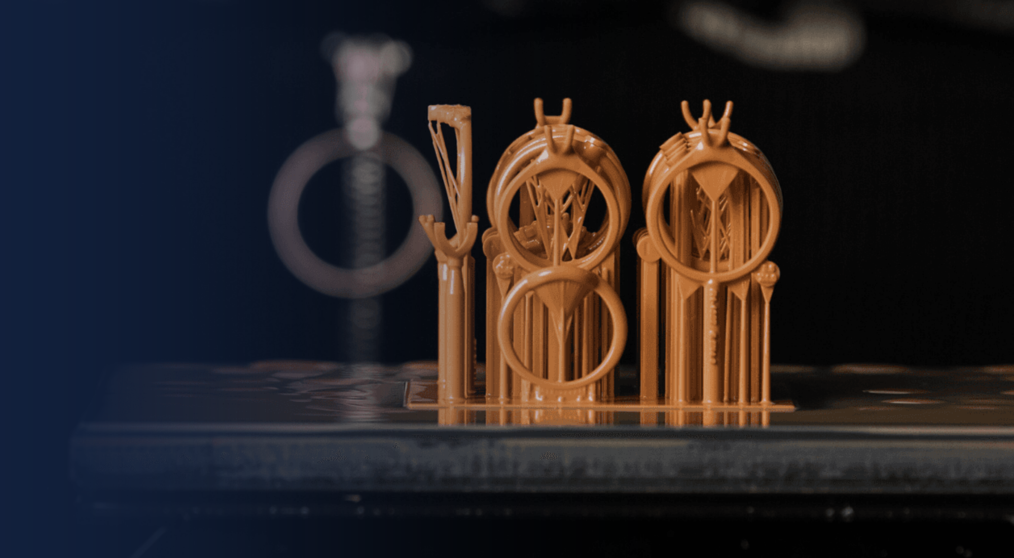 Several brown 3D-printed resin ring models standing on a build plate, held by a gloved technician.