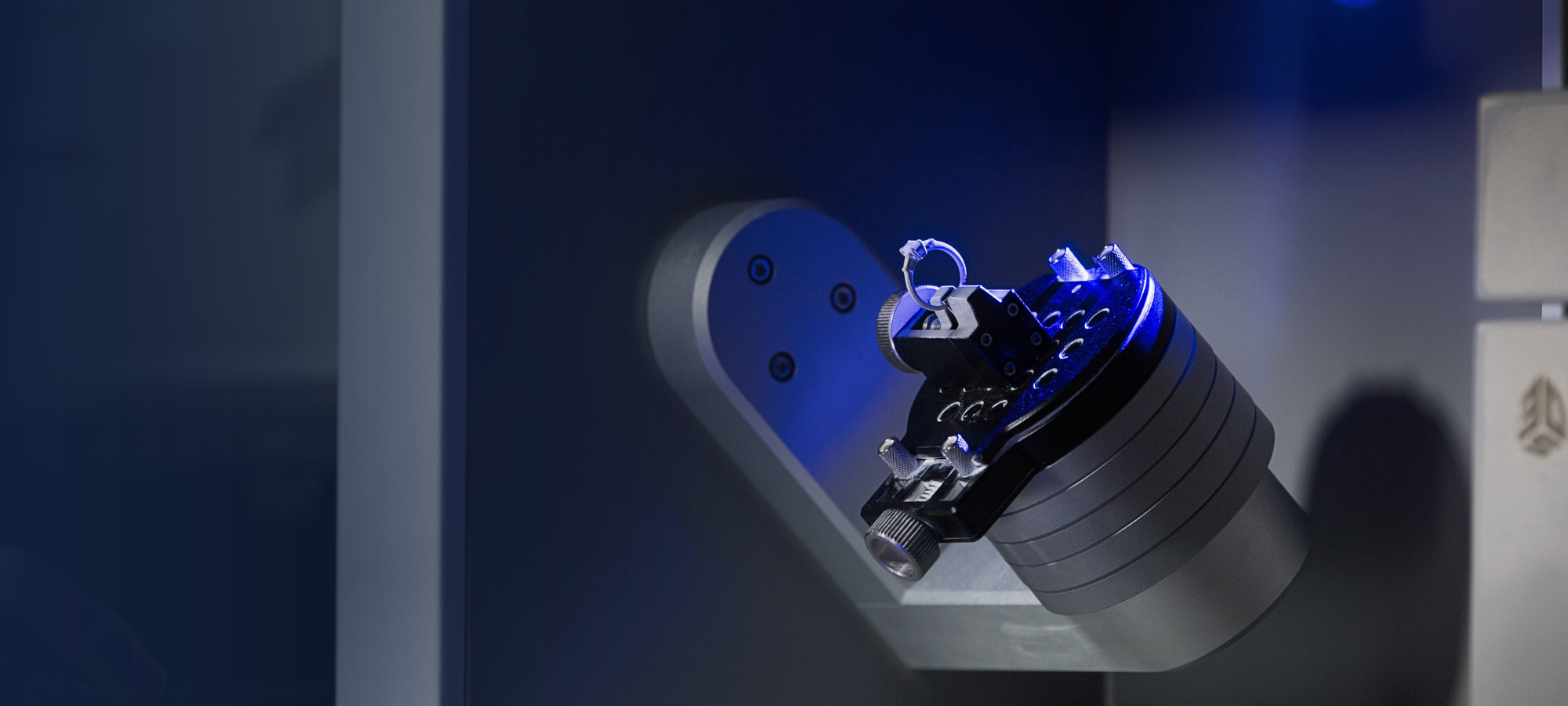 A small object is being scanned by a 3D scanner with a blue light. The object is a small model attached to a cylindrical base. The scanner is a white machine with "3D SYSTEMS" visible on the front.